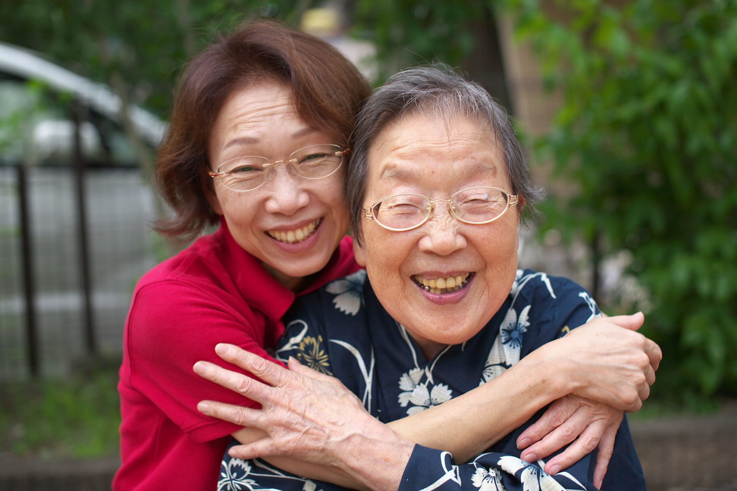 Two older women smiling and embracing outdoors